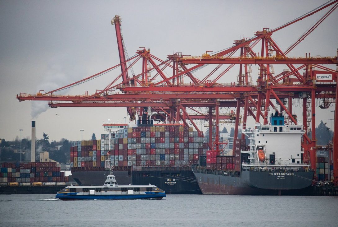 Gantry cranes tower above container ships being unloaded and loaded at port, in Vancouver